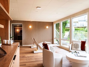 A modern hotel room with a wooden floor, a white sofa, a round table, and large windows offering a view of the outside.