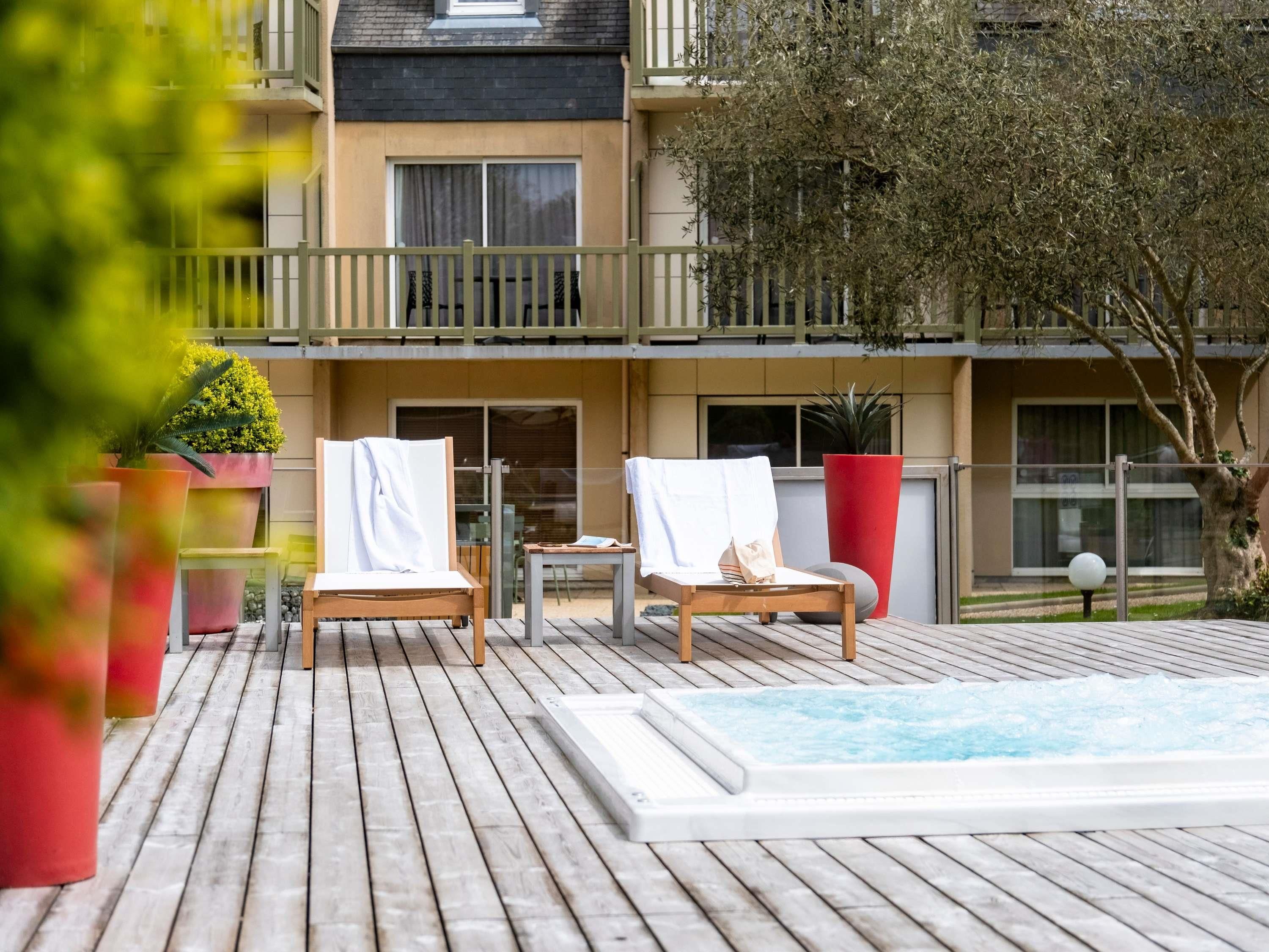 Una terraza de madera con dos tumbonas, una mesita y un jacuzzi.