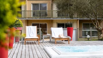 Una terraza de madera con dos tumbonas, una mesita y un jacuzzi.