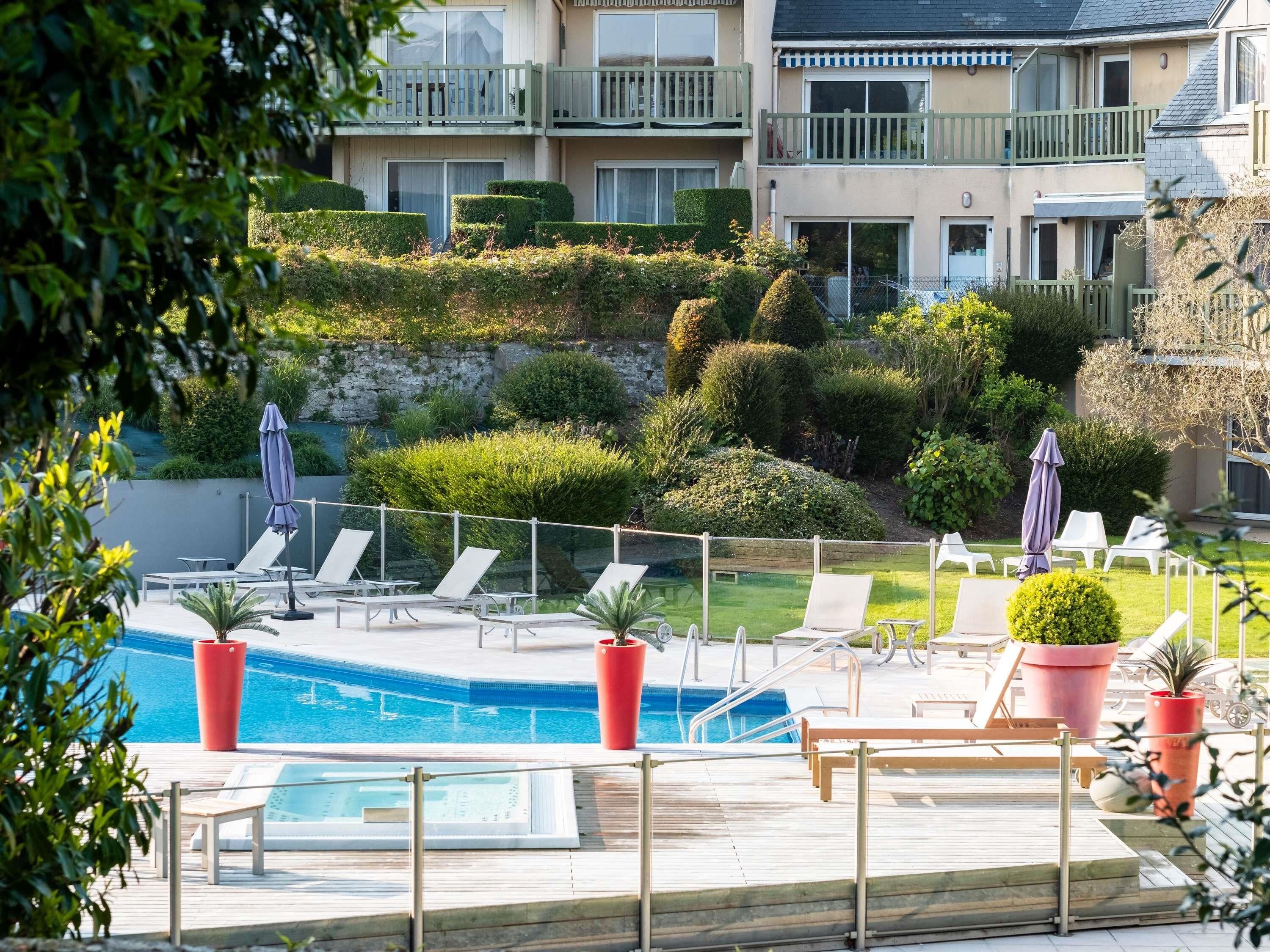 A pool area with lounge chairs, a small pool, and a view of a multi-story building with balconies.