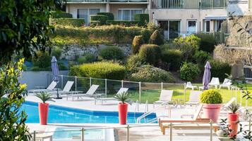 A pool area with lounge chairs, a small pool, and a view of a multi-story building with balconies.