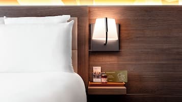 A neatly made bed with white linens, a bedside table with a lamp, a book, and a bottle.