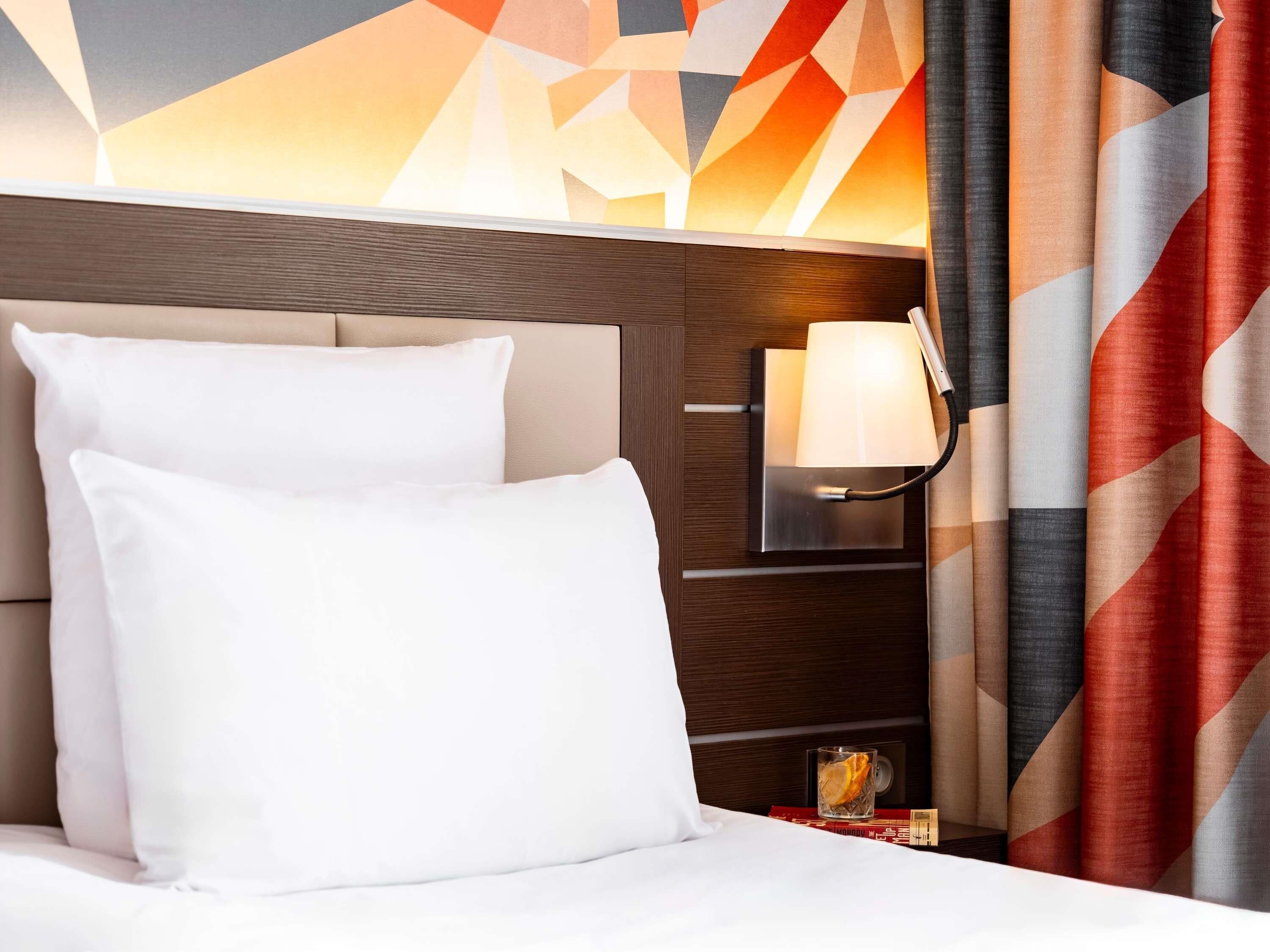 Une chambre d’hôtel avec un lit, une table de chevet, une lampe et un mur orné de motifs géométriques.