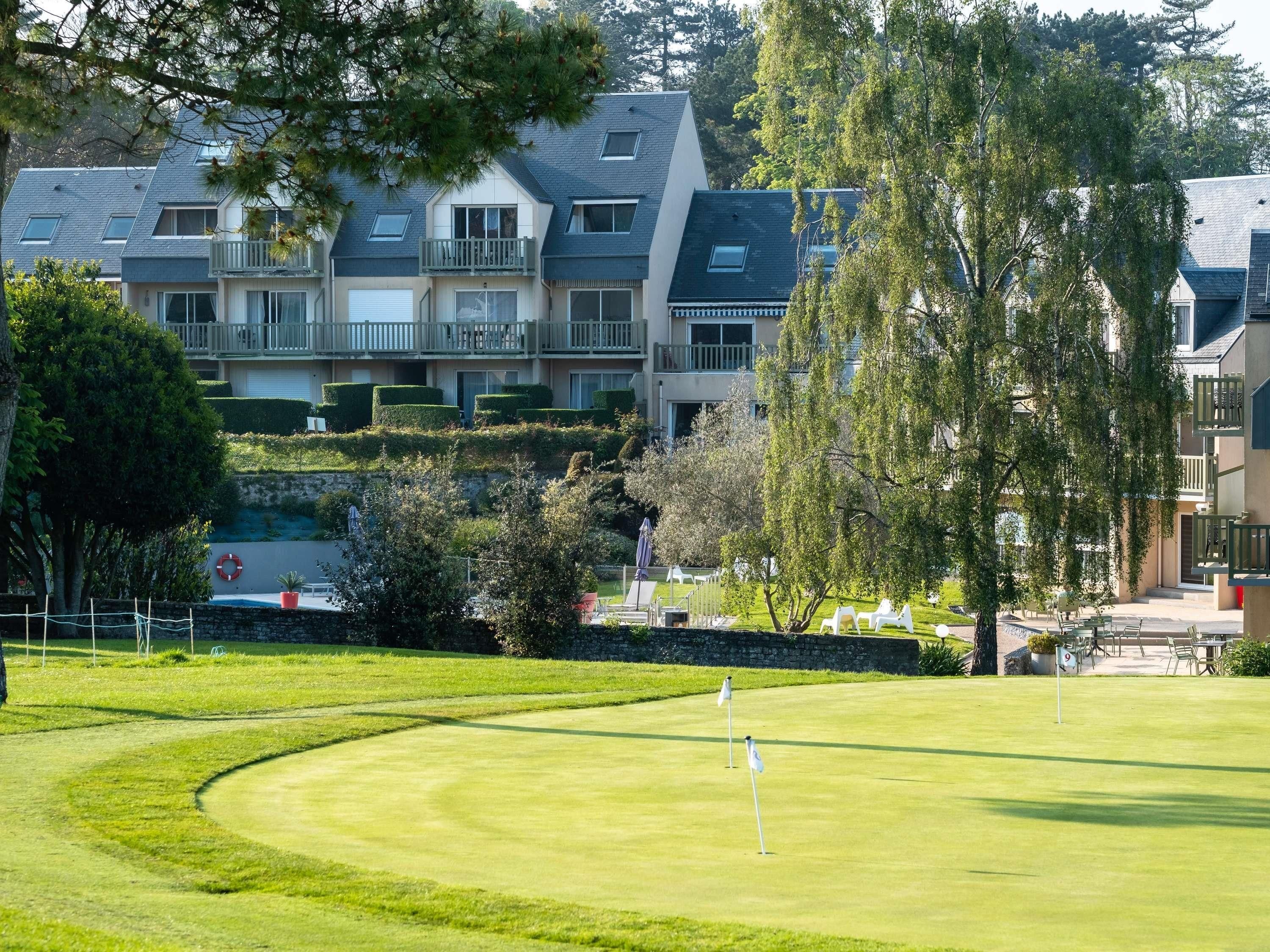 A golf course with a putting green, a flag, and a building with balconies in the background.