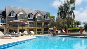 Un hotel con piscina, mobiliario exterior y un árbol grande.