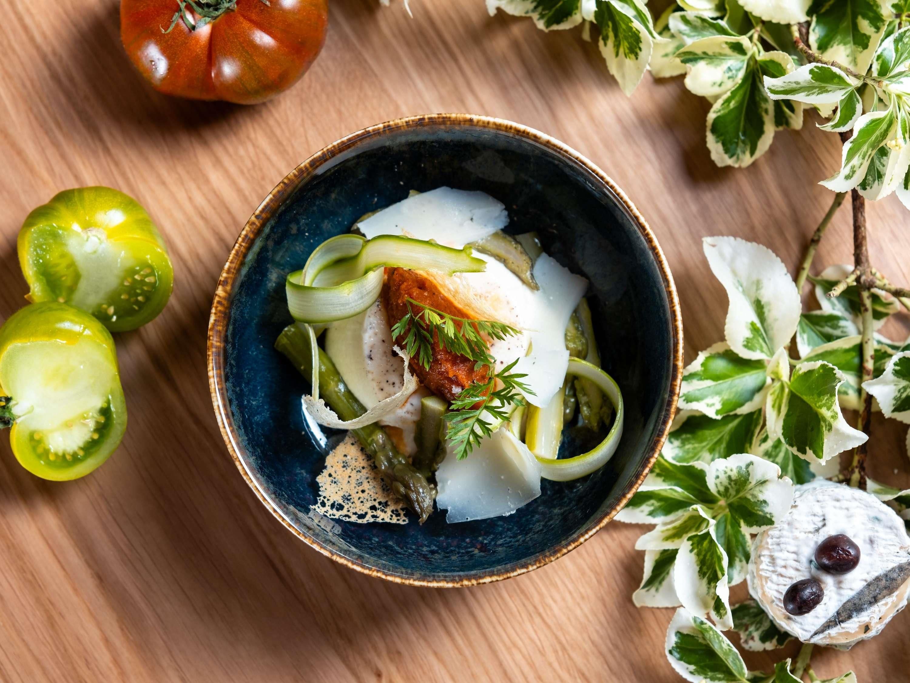 A bowl of food with vegetables and cheese on a wooden table.