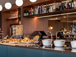 A bar area with shelves of liquor bottles, a coffee machine, and a buffet with bread and pastries. - Mercure Omaha Beach Hotel (Port-en-Bessin-Huppain)