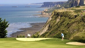 Un campo de golf con un marcador de bandera, búnkeres de arena y vistas al océano y acantilados.