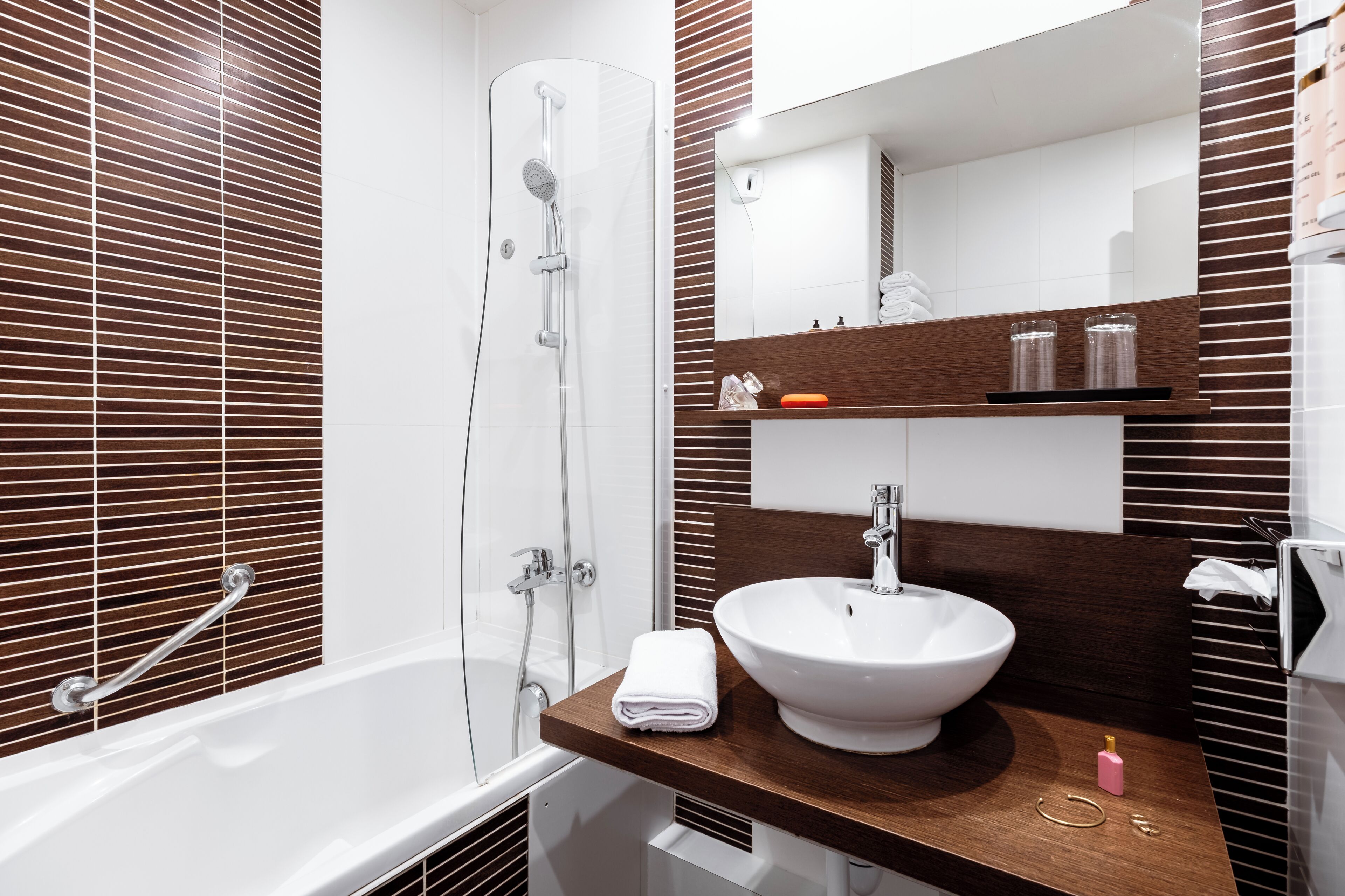 Une salle de bain moderne avec une baignoire, une douche à parois de verre, un meuble-lavabo en bois avec un lavabo blanc et un miroir au-dessus du meuble.