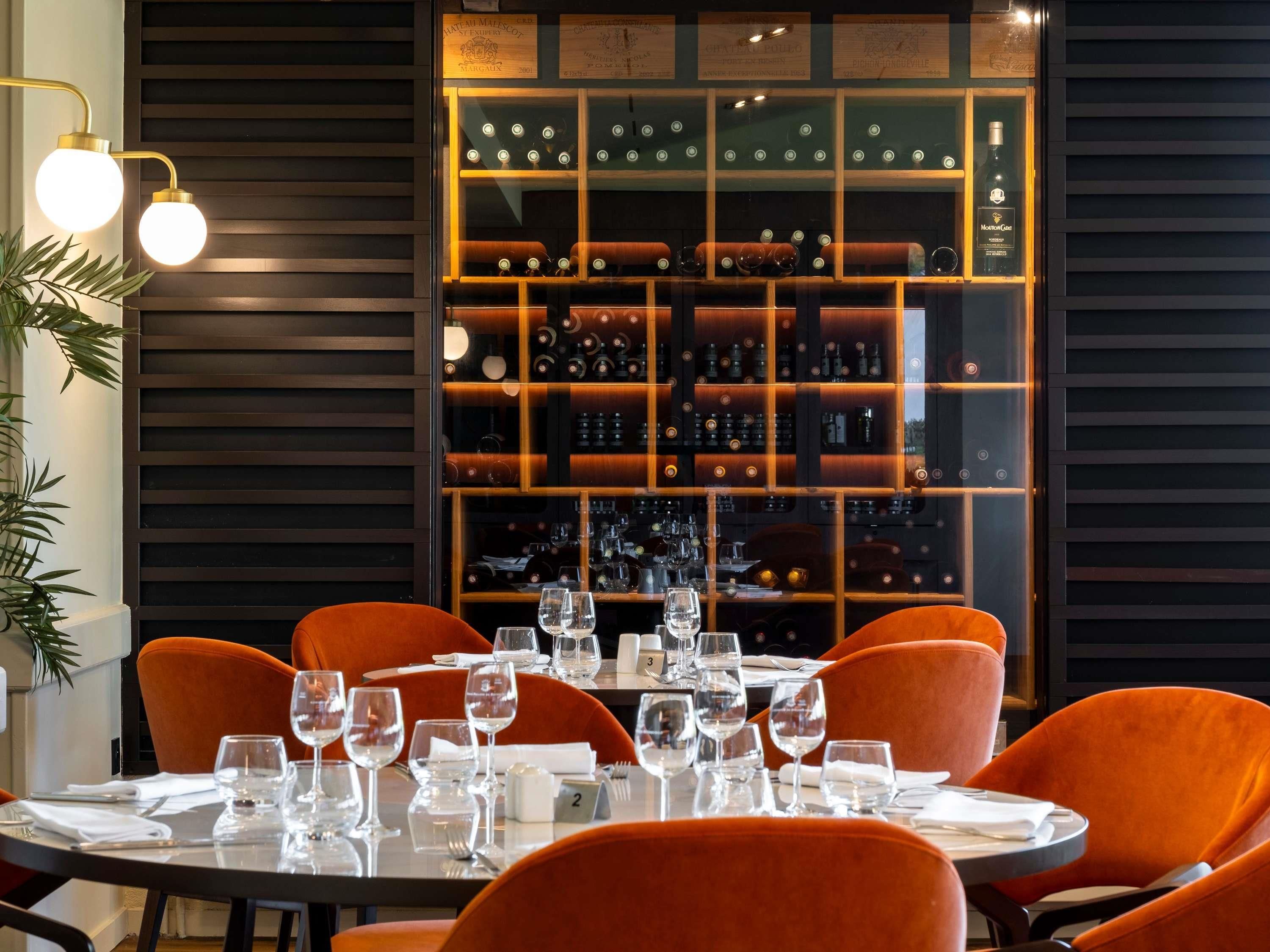 Un restaurante con una vitrina para vinos, sillas anaranjadas y una mesa preparada para comer.