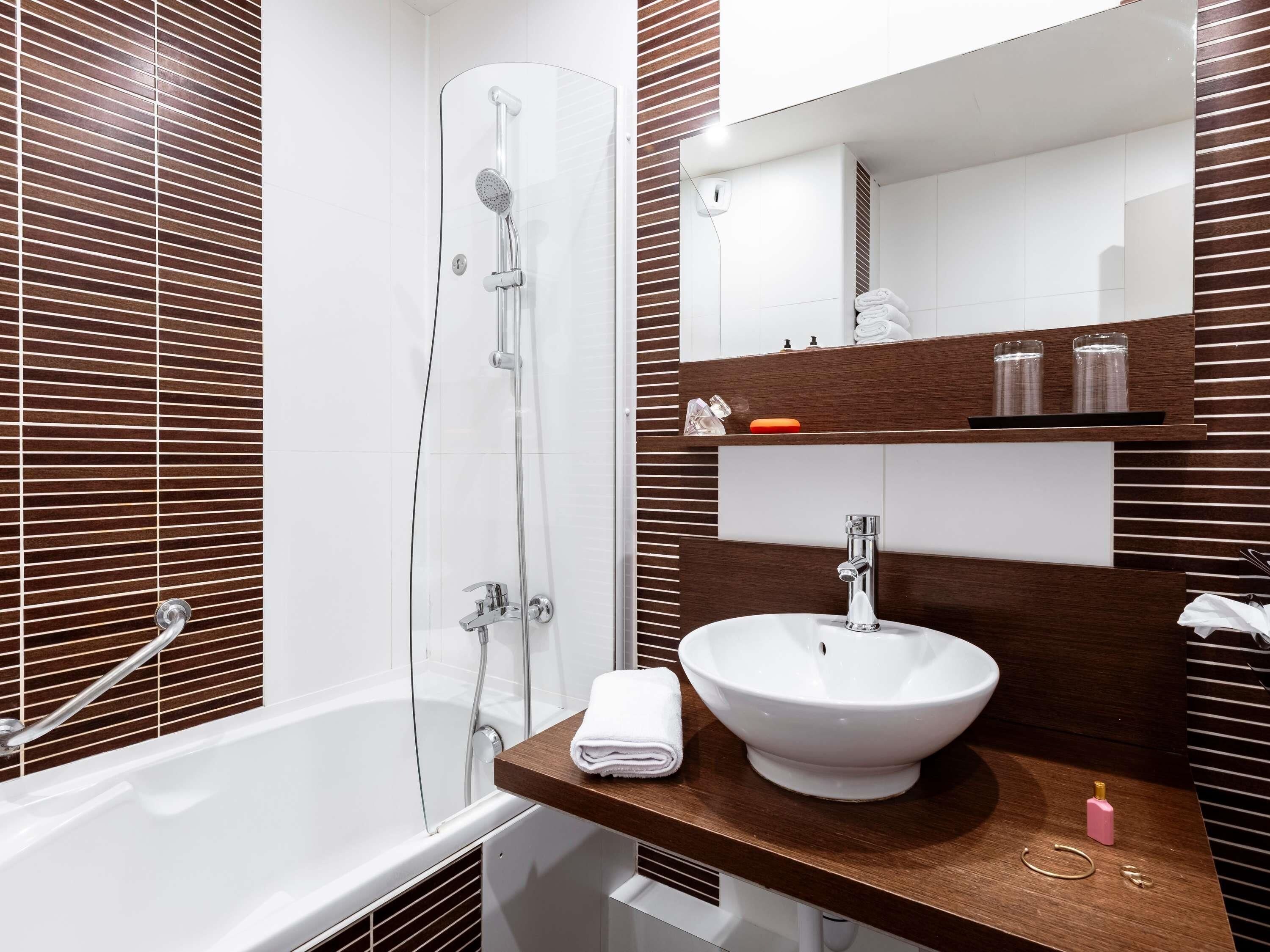 Ein modernes Badezimmer mit einer gläsernen Duschkabine, einer weißen Badewanne, einem hölzernen Waschtisch mit weißem Becken und einem Spiegel über dem Waschtisch.