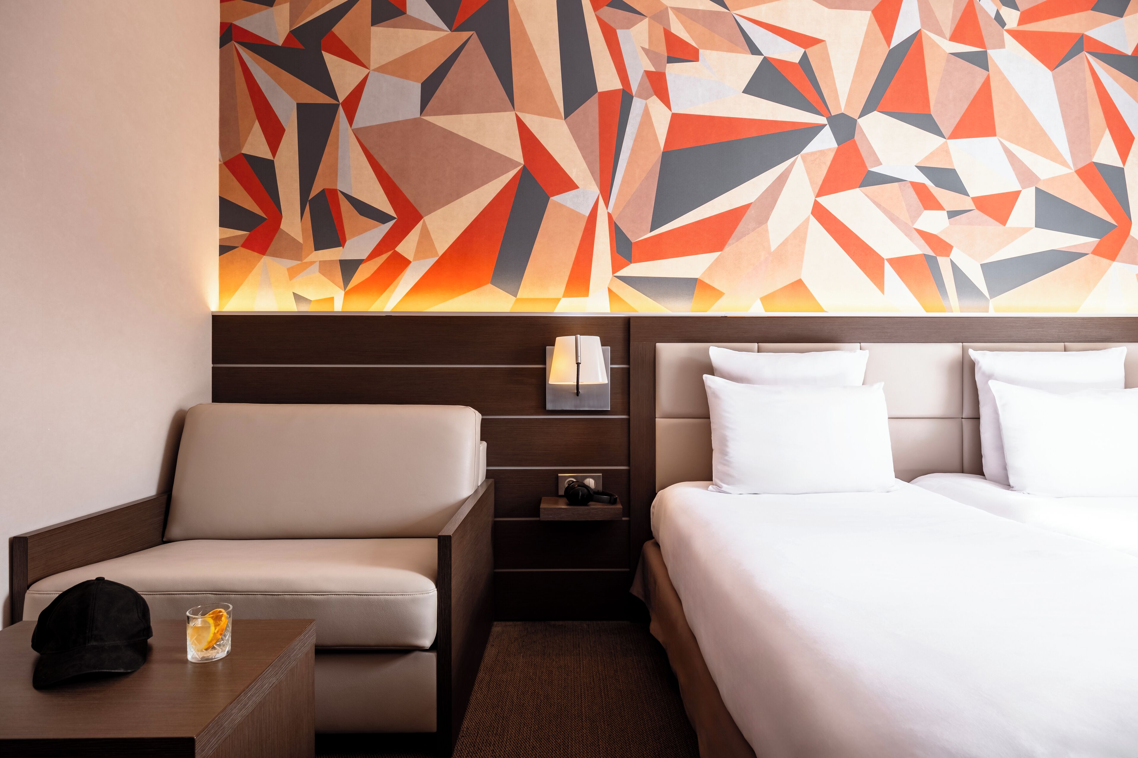 A hotel room with a bed, a sofa, a nightstand, and a wall art piece.
