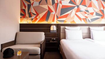 A hotel room with a bed, a sofa, a nightstand, and a wall art piece.