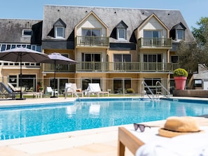 A hotel with a swimming pool, outdoor seating, and a large potted plant.