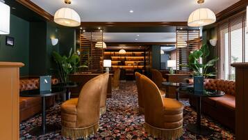 Un hall d’hôtel doté de sièges en cuir, d’un tapis à motifs et de luminaires suspendus.