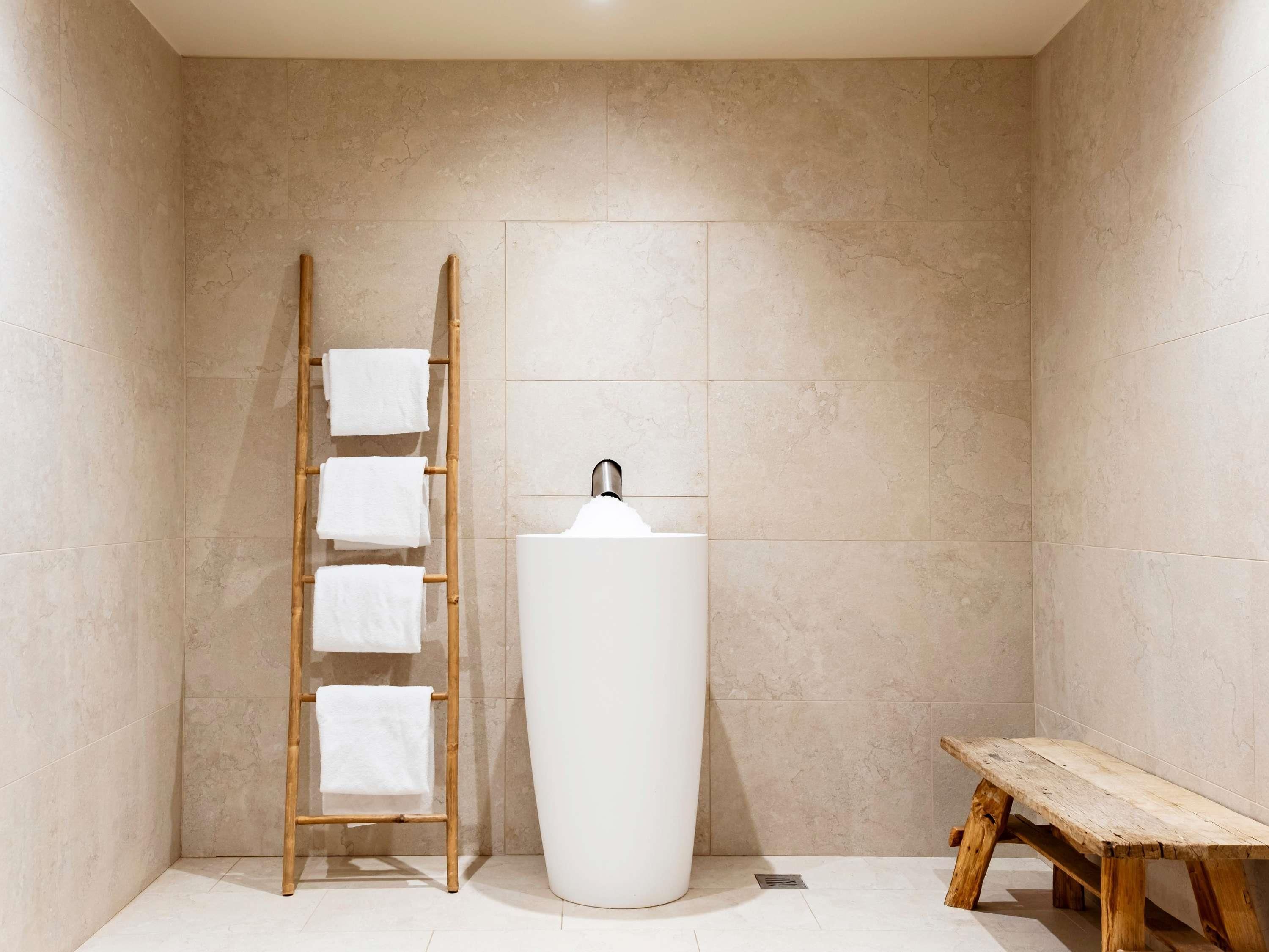 Une salle de bain avec un grand lavabo blanc, une échelle en bois sur laquelle sont posées des serviettes et un banc en bois.