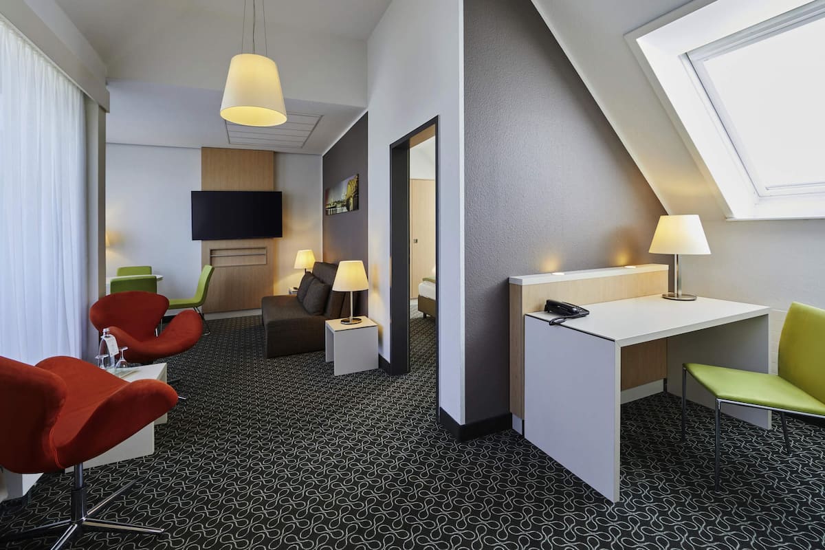 Een hotelkamer met een bureau, twee stoelen, een televisie, een telefoon en een kamerbreed tapijt met dessin.