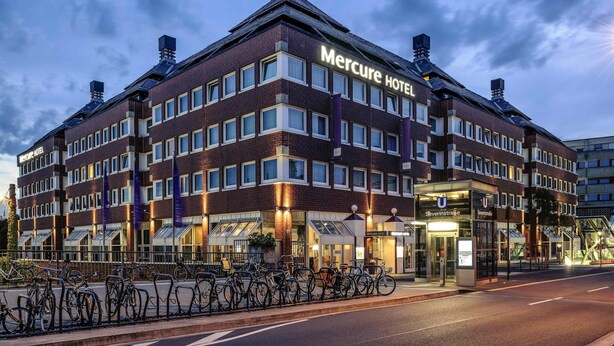 Un hôtel à plusieurs étages, reconnaissable à son grand panneau « Mercure Hotel », à son entrée en verre et à son espace de stationnement pour vélos.