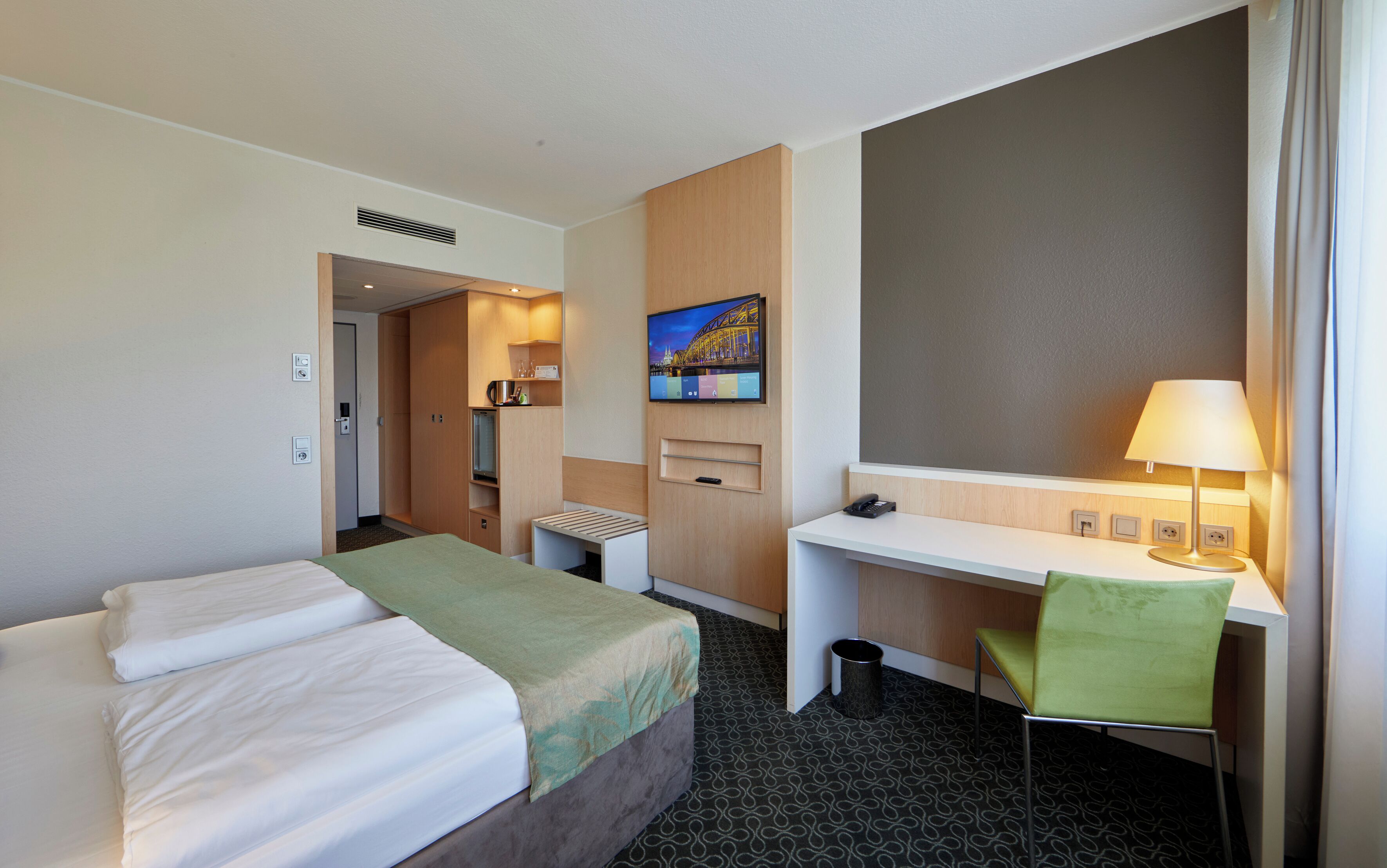 Habitación de hotel con cama, escritorio, silla y televisor en la pared.