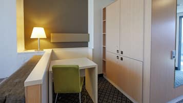 A small, modern room with a desk, a green chair, a lamp, and built-in wooden cabinets.