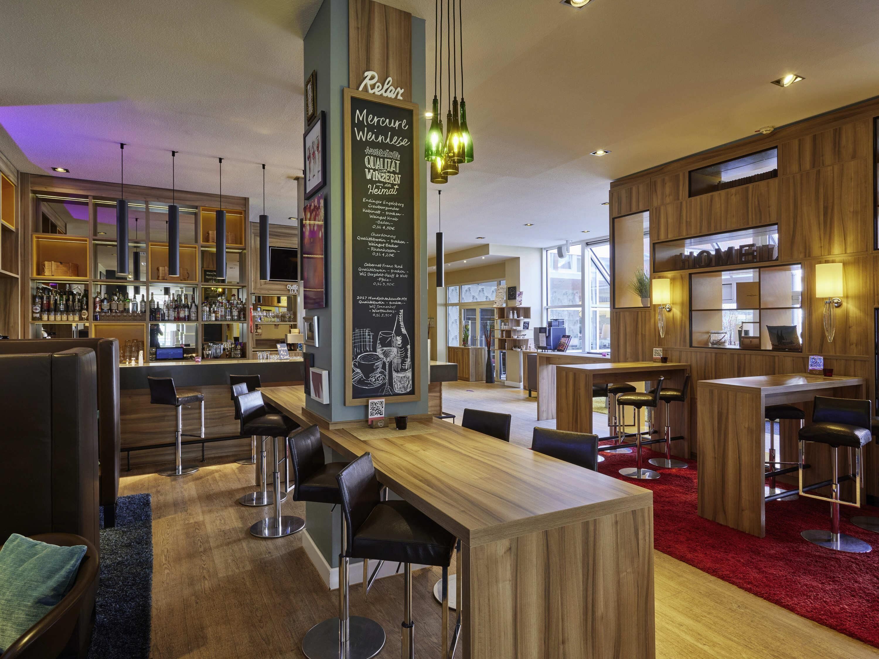 Un área de bar moderna con mobiliario de madera, un menú en una pizarra y vistas a la ciudad.