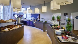 Un hall d'hôtel moderne doté d'un comptoir d'accueil incurvé, d'un espace dédié aux boissons chaudes et d'un buffet proposant une variété de plats.
