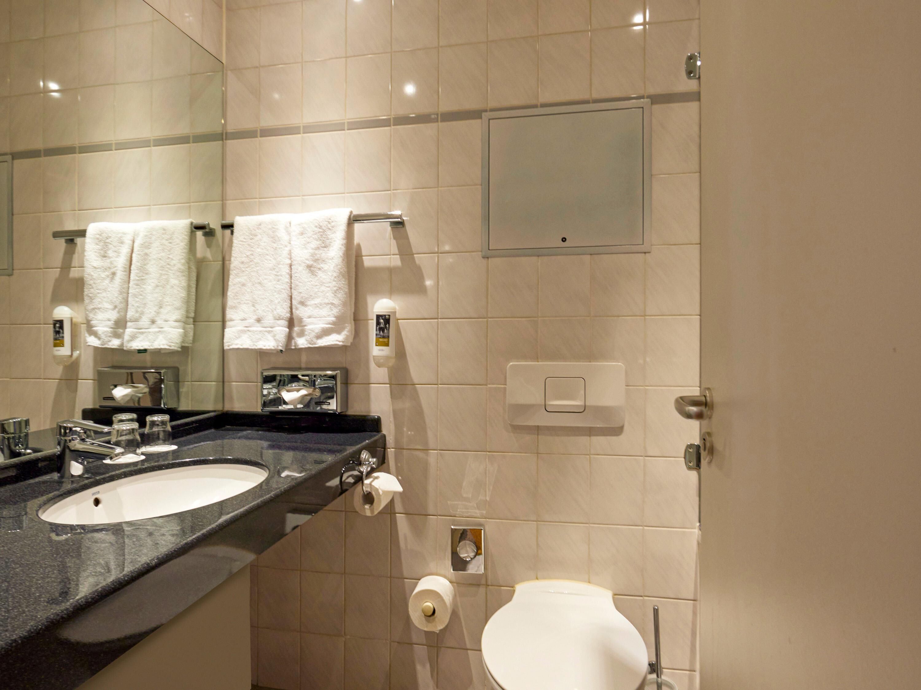 A bathroom with a sink, mirror, towel rack, toilet, and a soap dispenser.