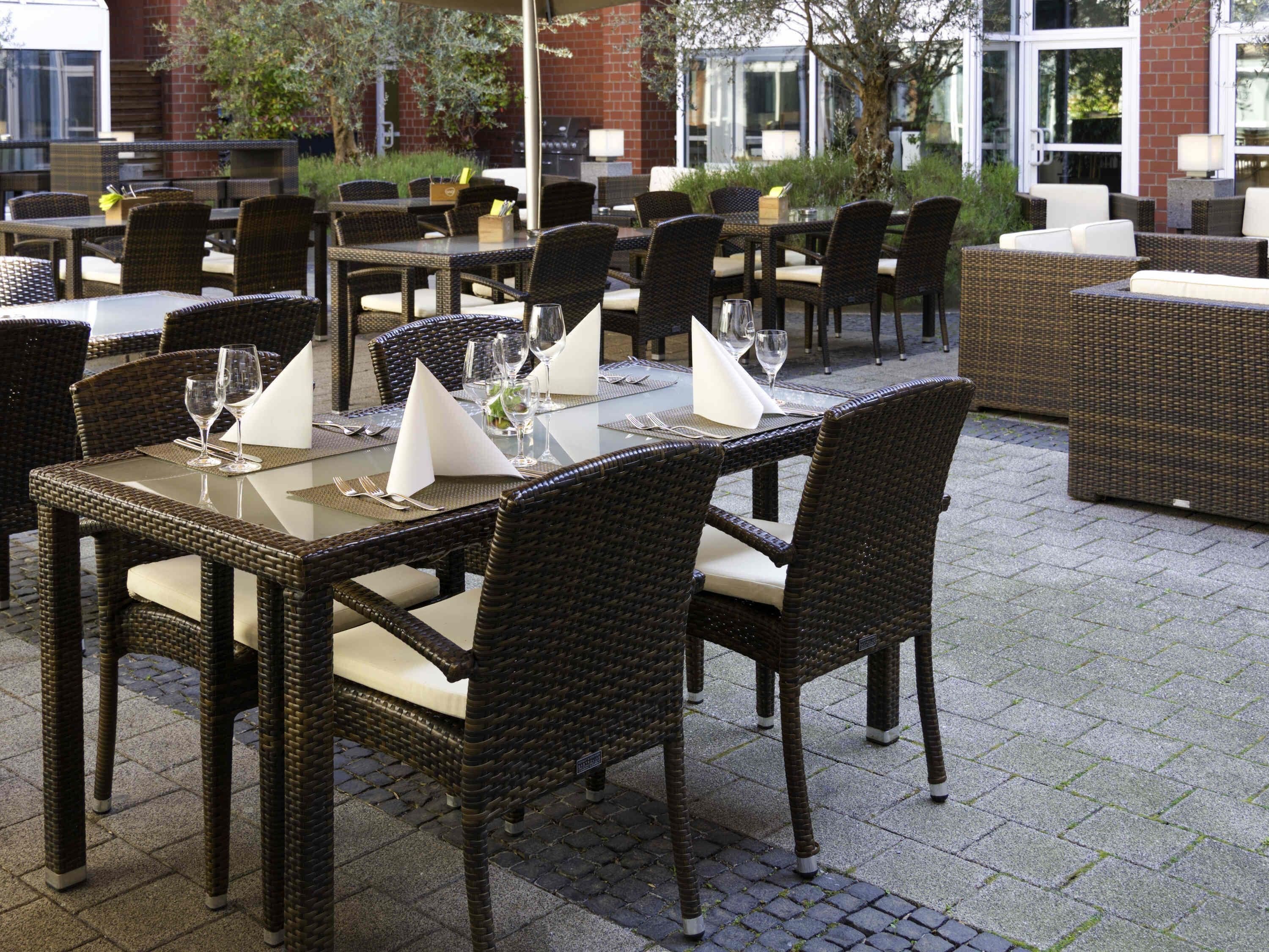 An outdoor dining area with wicker furniture and glass tables, set against a brick building.