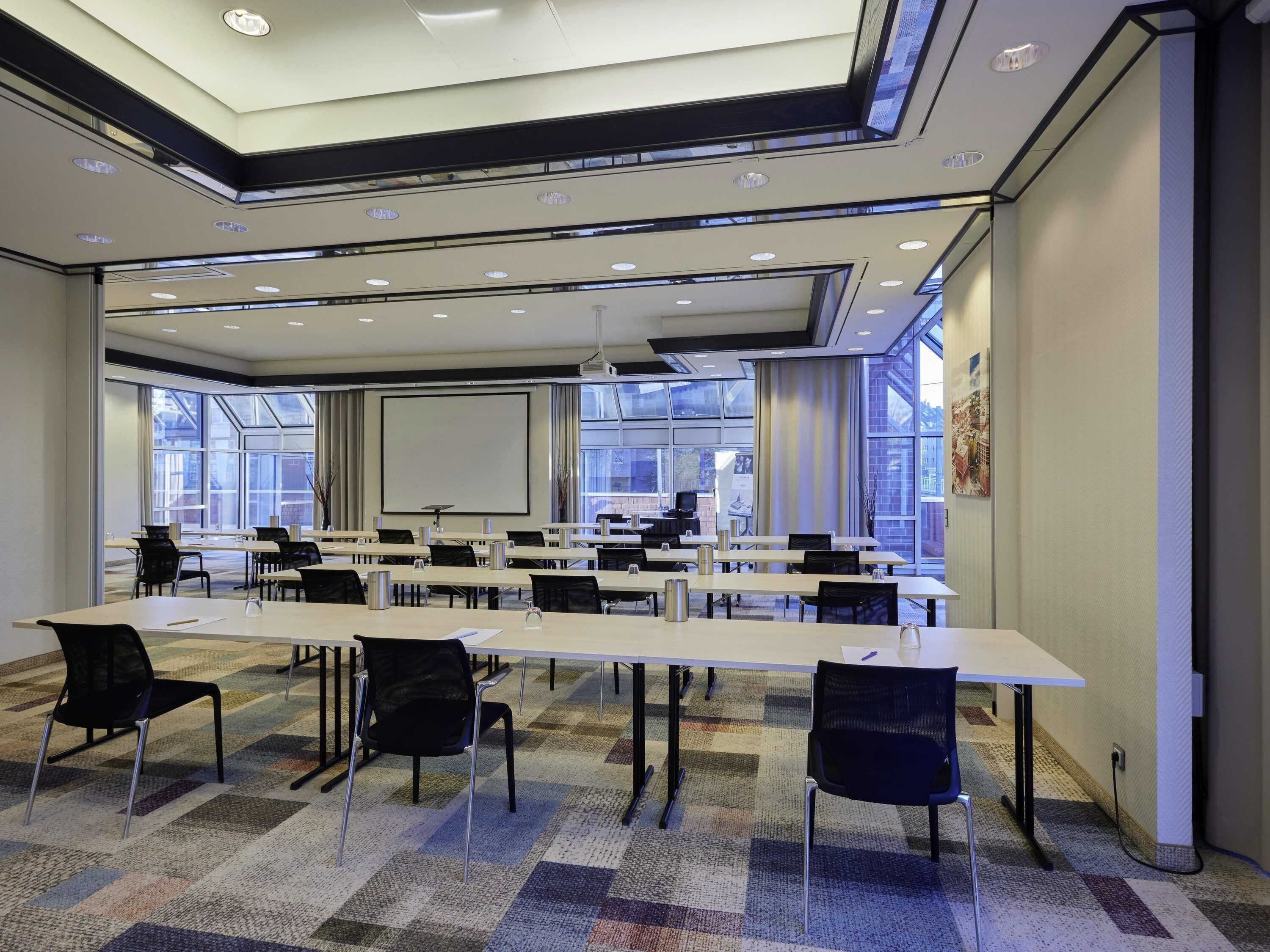 A conference room with tables, chairs, a projector screen, and large windows.