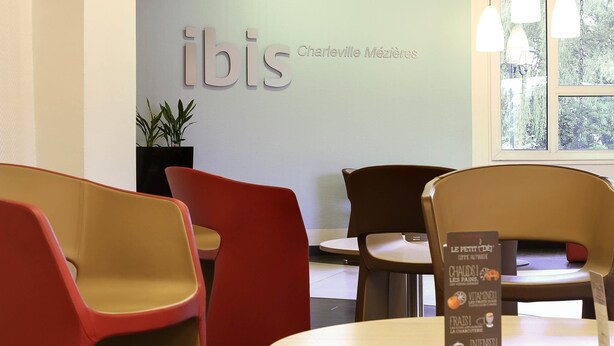 A modern interior with a sign reading "ibis Charleville Mézières". There are several chairs and a table with a menu. - ibis Charleville-Mezières (Villers-Semeuse)