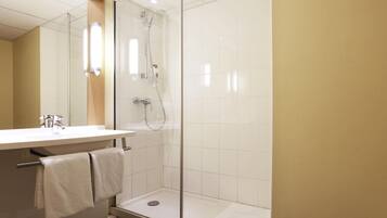 Un baño moderno con ducha de vidrio, lavamanos con espejo y toallero.