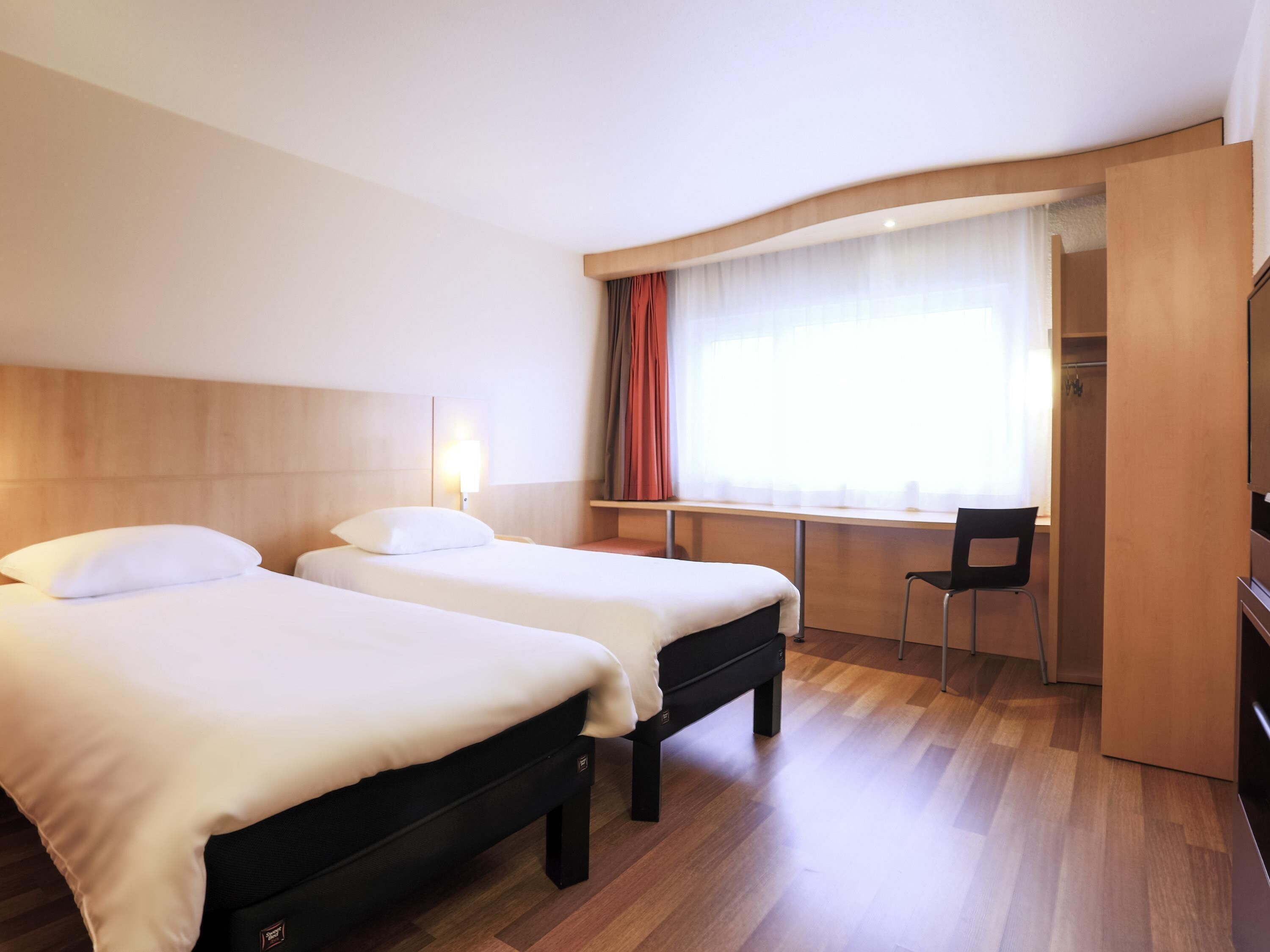Ett hotellrum med två sängar, ett skrivbord, en stol och en garderob.