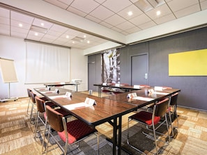 Un salón de conferencias con una larga mesa, sillas, una pantalla de proyector y un amplio ventanal.