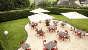 An outdoor patio with tables and chairs, surrounded by a hedge and houses in the background. - ibis Charleville-Mezières (Villers-Semeuse)