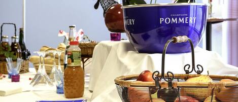 Una mesa con un tazón azul que dice 'POMMERY CHAMPAGNE', botellas, una cesta de frutas y diferentes botellas y copas.