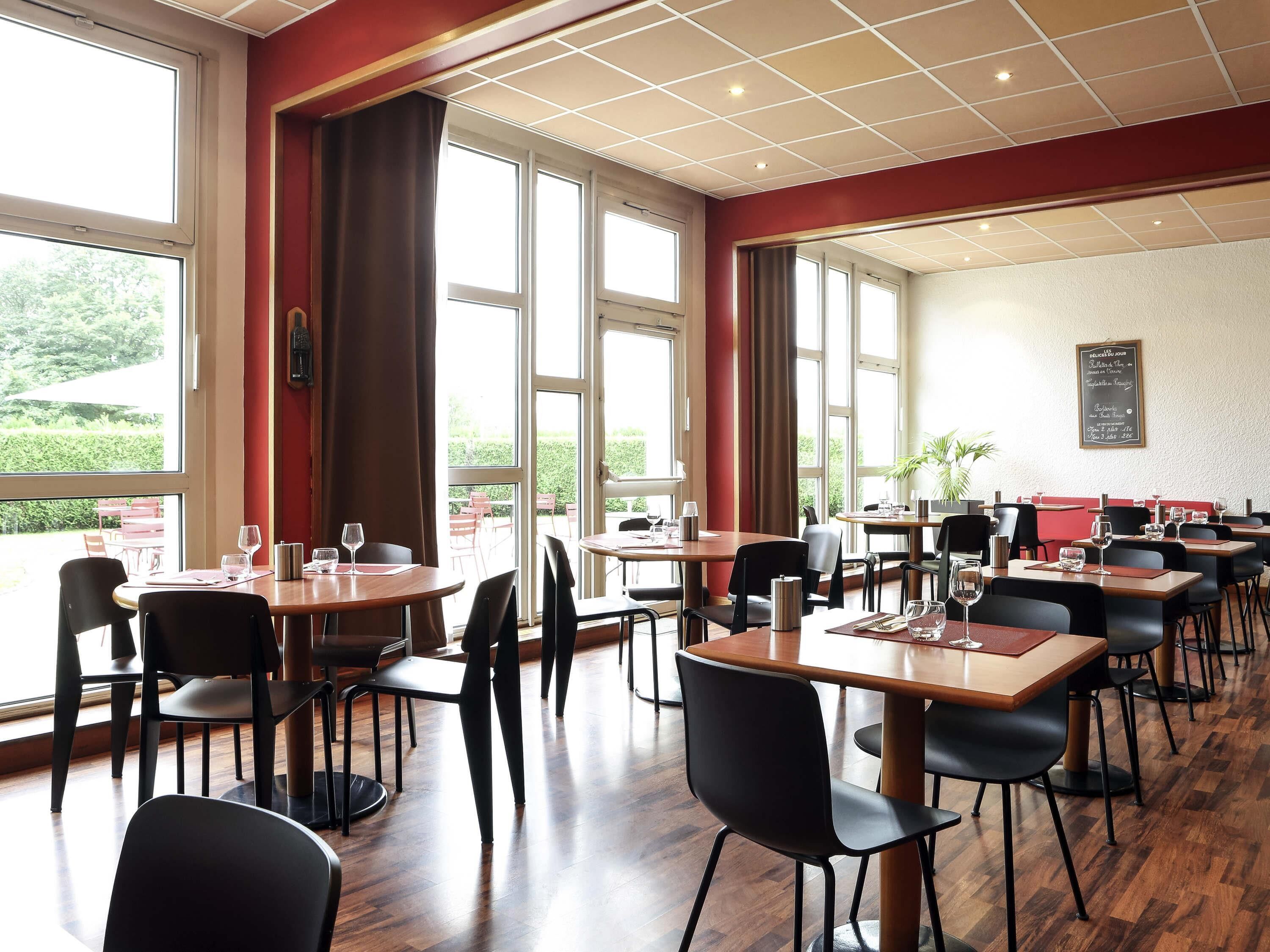 A restaurant with multiple tables and chairs, large windows, and a chalkboard menu.