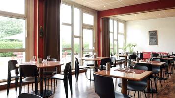A restaurant with multiple tables and chairs, large windows, and a chalkboard menu.