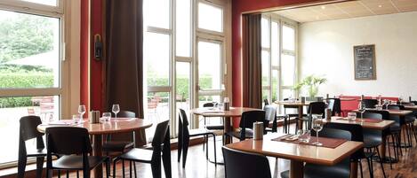 A restaurant with multiple tables and chairs, large windows, and a chalkboard menu.