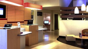 A reception area with a wooden reception desk, a computer, and a seating area with a round table and chairs. - ibis Charleville-Mezières (Villers-Semeuse)