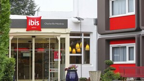 A hotel entrance with a red sign, glass doors, and a potted plant. - ibis Charleville-Mezières (Villers-Semeuse)