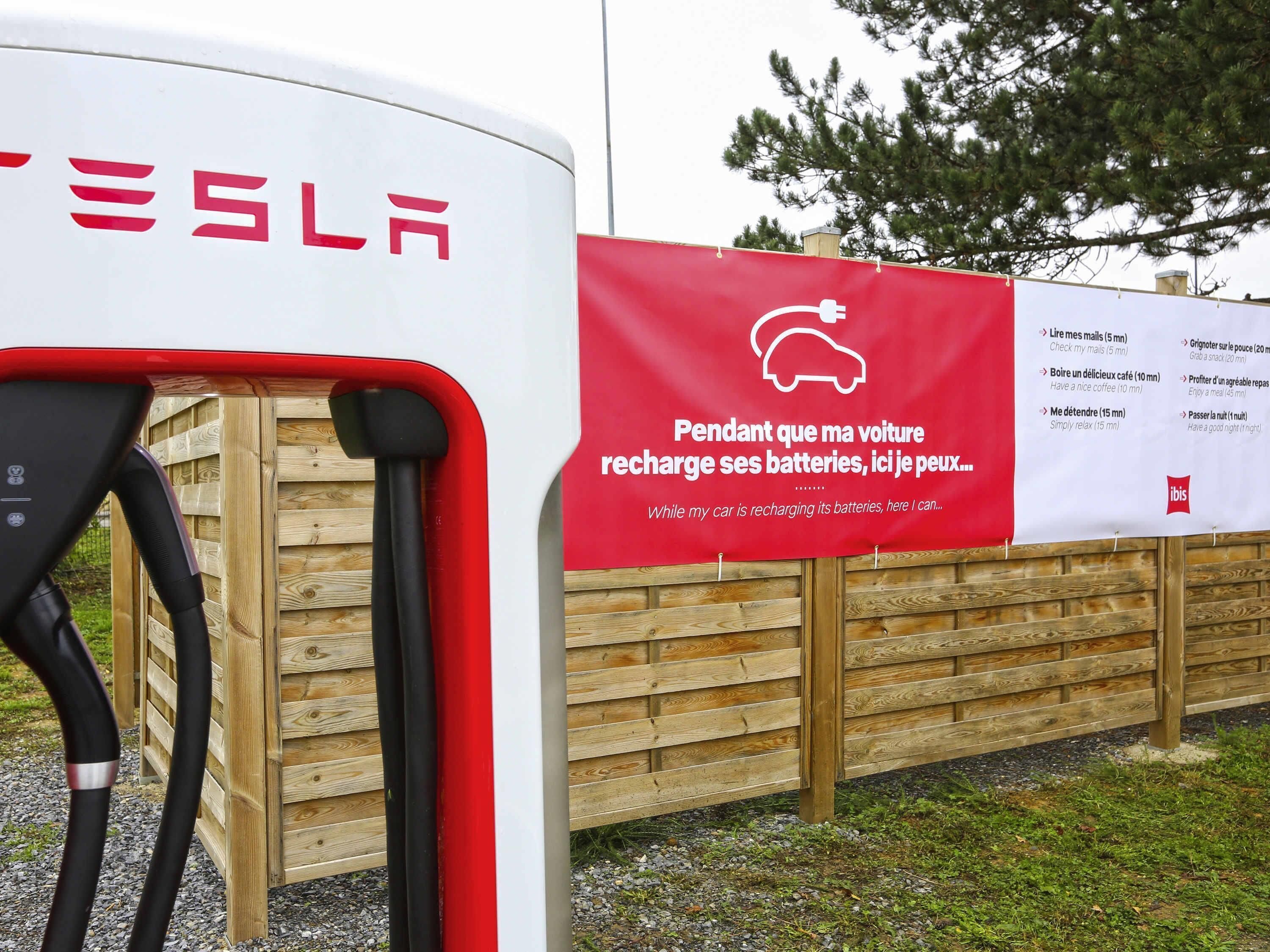 En Tesla-laddstation med en röd banner som annonserar en tjänst medan bilen laddas.