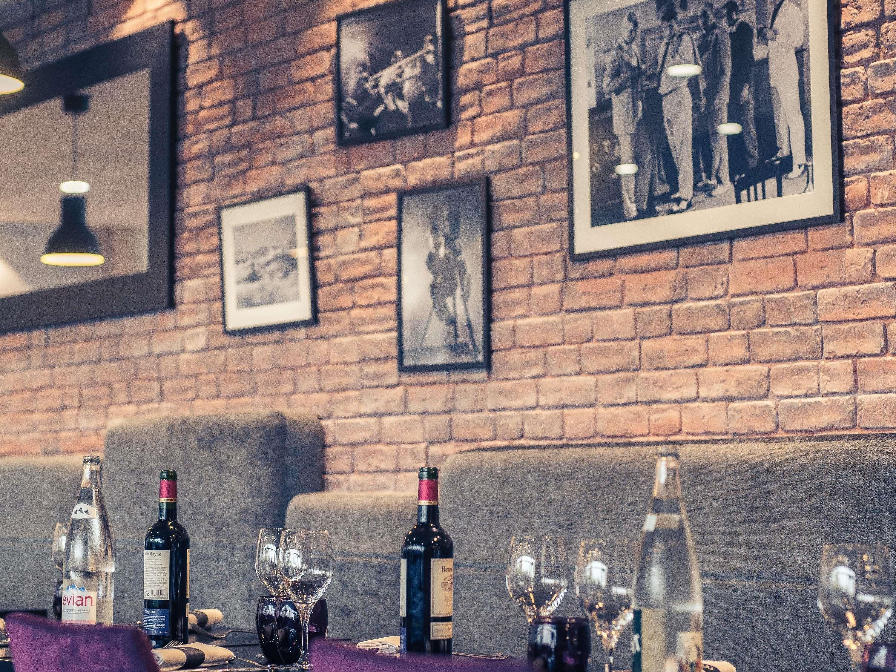 A restaurant interior with brick walls, framed black and white photographs, and a table set with wine bottles and glasses.