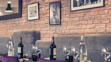A restaurant interior with brick walls, framed black and white photographs, and a table set with wine bottles and glasses.
