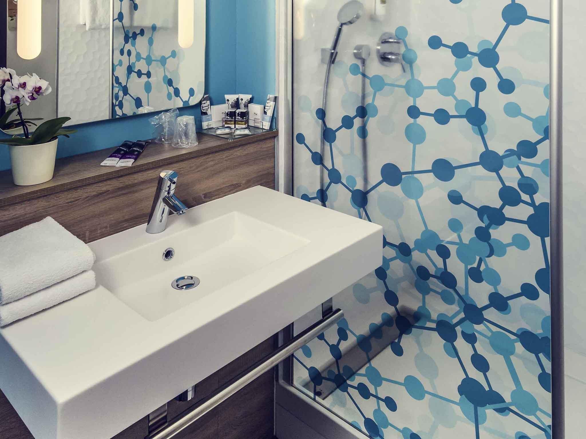 A bathroom with a white sink, a mirror, and a shower with a blue molecular pattern wall.
