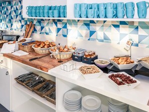 Montaje de bufé con diversos alimentos, utensilios y vasos azules sobre estantes.