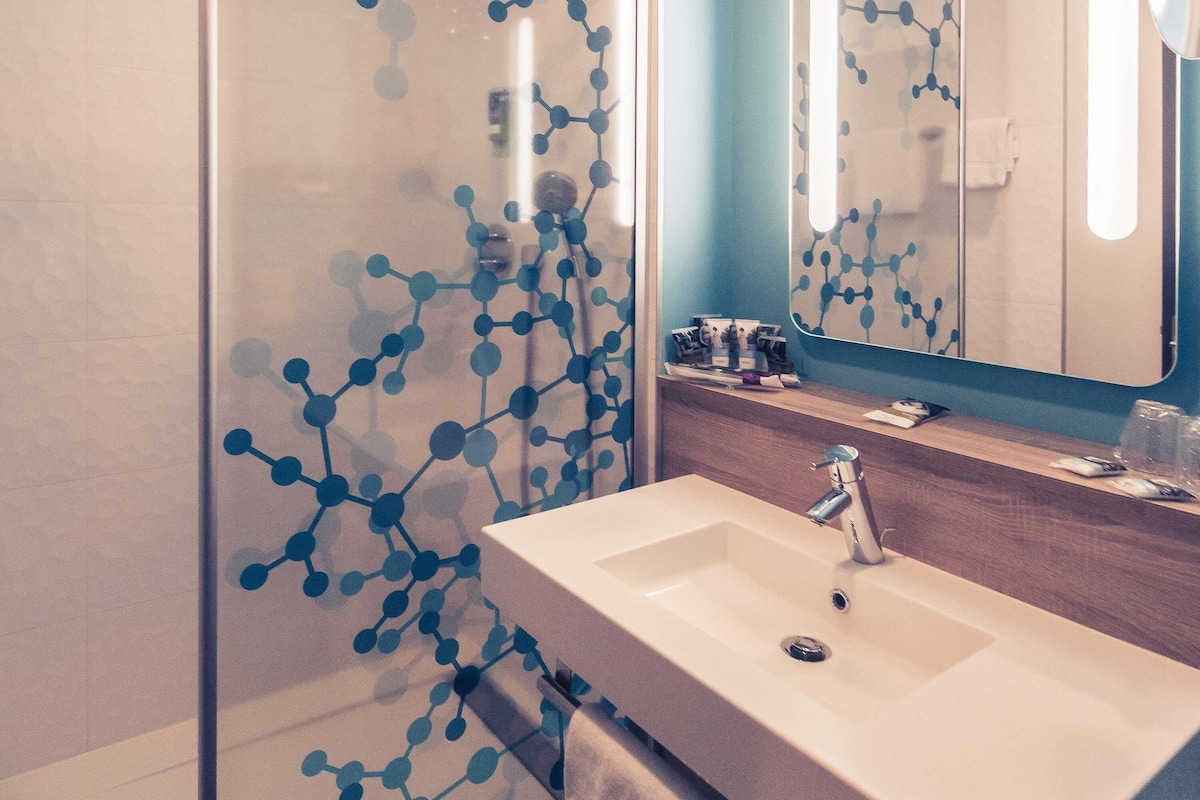 A bathroom with a white sink, a mirror, and a glass partition with a blue molecular pattern.