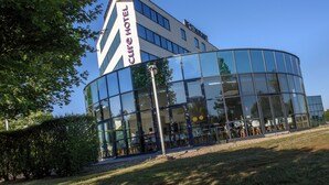 A modern hotel with a curved glass facade, a prominent logo, and a well-maintained outdoor seating area. - Mercure Poitiers Site du Futuroscope Hotel (Chasseneuil-du-Poitou)