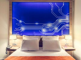 Una habitación de hotel con una cama, dos mesitas de noche, un teléfono y una pared con un diseño de placa de circuito azul.