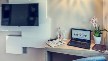 Ein modernes Hotelzimmer mit Flachbildfernseher, Laptop, Zeitschrift, Flasche, Glas und einer Topfpflanze Orchidee.