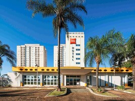 Un hotel de diseño moderno, con un llamativo letrero de 'ibis', una entrada central y palmeras alrededor.